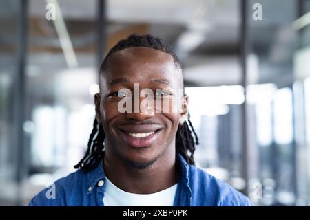 Junger afroamerikanischer Mann lächelt in Büroumgebung mit Glaswänden, Geschäft Stockfoto