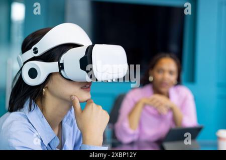 Asiatische junge Frau verwendet VR-Headset als birassische junge Frau beobachtet und arbeitet an Geschäften zusammen Stockfoto
