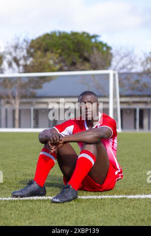 Junger afroamerikanischer Athlet in roter Sportbekleidung, der auf dem Fußballfeld ruht Stockfoto