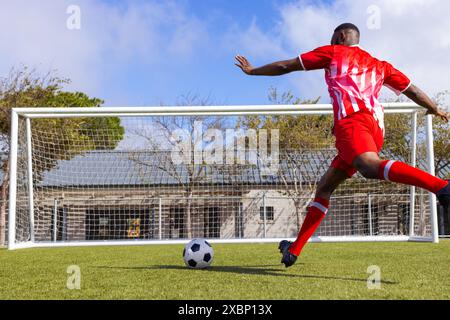 Afroamerikanischer Fußballspieler, der am sonnigen Tag den Fußball in Richtung Tor kippt, Kopierraum Stockfoto