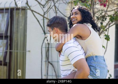 Junger kaukasischer Mann, der eine asiatische Frau mit Huckepack reitet, sowohl lächelnd als auch lustig Stockfoto