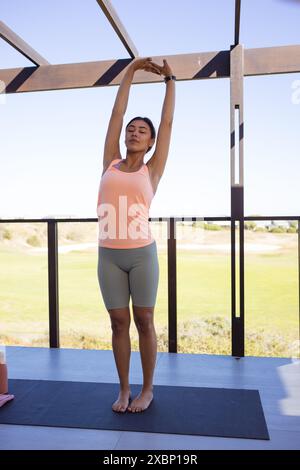 Glückliche birassische Frau, die Yoga auf Yogamatte macht, sieht entspannt und fit aus Stockfoto