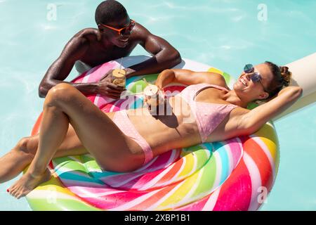 Ein vielseitiges Paar, das sich auf dem farbenfrohen Schwimmbecken entspannt und Drinks genießt Stockfoto