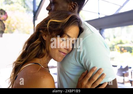 Glückliche kaukasische Frau umarmt den Afroamerikaner, die Augen geschlossen und lächelnd, zu Hause Stockfoto