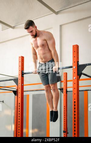 Fokussierter Mann, der Calisthenics-Muskel in hoher Position auf Metallstange in modernen Fitnessraum durchführt Stockfoto