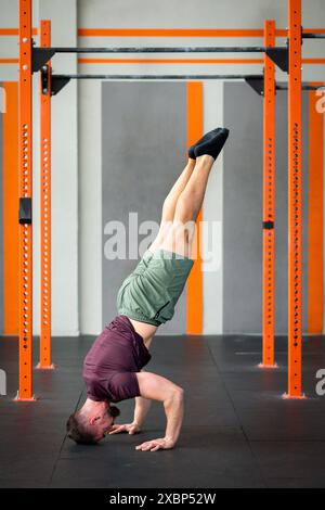 Ganzkörper-Seitenansicht eines fitten männlichen Athleten, der tagsüber auf dem Boden im Fitnessstudio eine Calisthenics-Stativ-Kopfstand-Übung macht Stockfoto