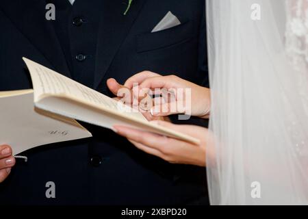 Braut und Bräutigam halten Hände und lesen während einer religiösen Zeremonie ihr Ehegelübde aus einem Buch Stockfoto