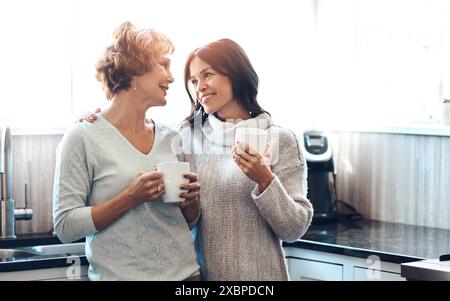 Liebe, Kaffee und Mutter im Gespräch mit der Tochter in der Küche, Morgen und Unterstützung für die Erziehung. Glücklich, lächelnd und weiblich mit reifer Mutter Stockfoto