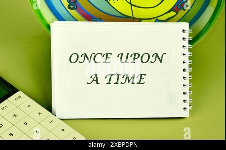 Es war einmal ein Text auf einem Notizblock auf dem Hintergrund einer Uhr neben einem Rechner Stockfoto