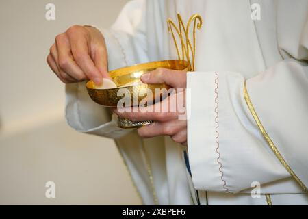 Priester auf einer weißen alb, die mit goldenen Ornamenten geschmückt ist und einen goldenen Kelch mit geweihten Wirten während einer Massenfeier hält Stockfoto