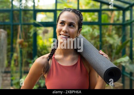 Birassisch geschnittene Frau, die Yogamatte hält und in die Kamera lächelt Stockfoto