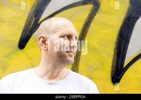 Glatzkopf in weißem T-Shirt, seitlich aussehend, farbenfroher Graffiti-Hintergrund, urbane Umgebung Stockfoto