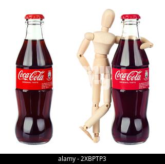 Set aus Coca-Cola-Flasche und hölzerner Puppe umarmen sie, isoliert auf weißem Hintergrund. Coca-Cola, oder Cola, ist ein kohlensäurehaltiges Erfrischungsgetränk Stockfoto