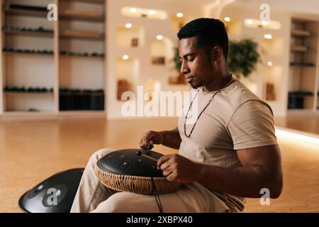 Fokussierter schwarzer Schlagzeuger in Trance, der mit Drumsticks auf Glucophon spielt und im gemütlichen Meditationsraum im Kreuz auf dem Boden sitzt. Konzept von Stockfoto