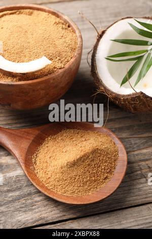 Kokosnusszucker in Schüssel, Löffel, Obst und Palmblätter auf Holztisch, Nahaufnahme Stockfoto