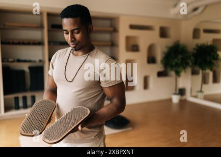 Porträt eines gutaussehenden afrikanischen Mannes, der ein hölzernes Sadhu-Brett in Händen hält, mit Nägeln, die im gemütlichen Wohnzimmer stehen und sich auf das Üben vorbereiten. Konzept von Stockfoto