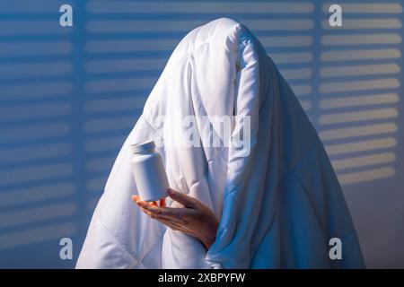 Schlafkapsel in der Hand, unerkennbarer Mann unter einer Decke, Melatonins Kampf gegen Schlaflosigkeit Stockfoto