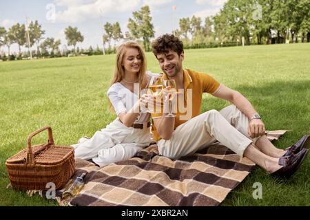 Ein eleganter Mann und eine elegante Frau in stilvollen Outfits, die auf einer Decke neben einem Picknickkorb in einem üppigen Park sitzen. Stockfoto