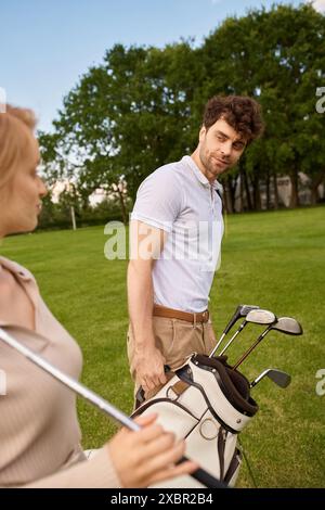 Ein junges Paar in eleganter Kleidung steht Seite an Seite auf einem Golfplatz, umgeben von üppigem Grün. Stockfoto