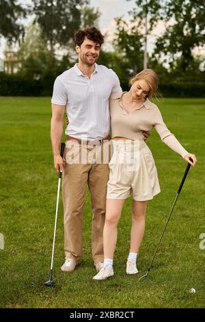 Ein junger Mann und eine Frau in eleganter Kleidung posieren liebevoll auf einem Golfplatz, der unter dem klaren Himmel liegt. Stockfoto