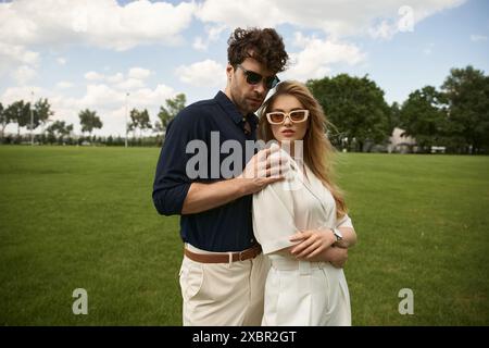 Ein Mann und eine Frau, elegant gekleidet, stehen zusammen in einem üppigen grünen Feld und verkörpern ein Leben voller Luxus und Raffinesse. Stockfoto