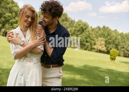 Ein wunderschönes junges Paar in eleganter Kleidung, das sich zärtlich in einem grünen Feld umarmt und Liebe und Gelassenheit verkörpert. Stockfoto