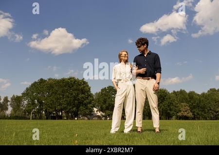 Ein stilvoller junger Mann und eine Frau in eleganter Kleidung stehen Seite an Seite auf einem üppig grünen Feld. Stockfoto