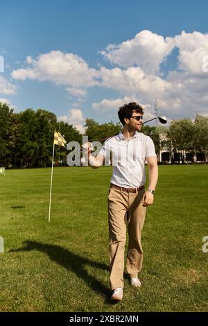 Ein stilvoller Mann, der über einen Golfplatz schlendert, einen Golfclub hält und einen entspannten Tag in einer üppigen grünen Umgebung genießt. Stockfoto