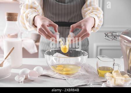 Teig herstellen. Frau bricht Ei am weißen Tisch in der Küche, Nahaufnahme Stockfoto