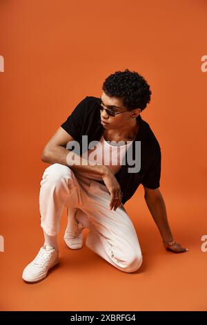 Schöner afroamerikanischer Mann in stilvoller Sonnenbrille, der auf orangefarbenem Hintergrund hockt. Stockfoto