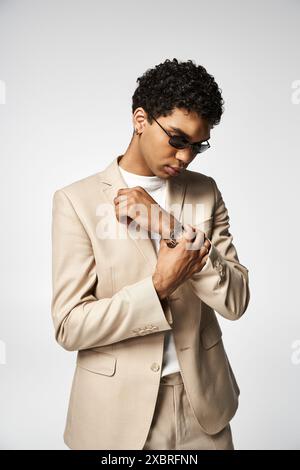 Schöner afroamerikanischer Mann in einem braunen Anzug und einer stilvollen Sonnenbrille, die seine Uhr anpasst. Stockfoto