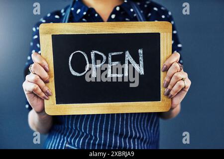 Frau, Hände und Tafel mit offenem Schild zur Begrüßung oder Einführung im Studio. Nahaufnahme einer weiblichen Person oder Kellnerin mit Plakatwand oder Stockfoto
