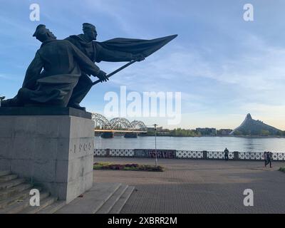 Riga, Lettland, 2. Mai 2024: Nahaufnahme des Denkmals der Kämpfer von 1905 am Fluss Daugava mit Blick auf die neue Bibliothek und Eisenbahnbrücke in Riga. Stockfoto