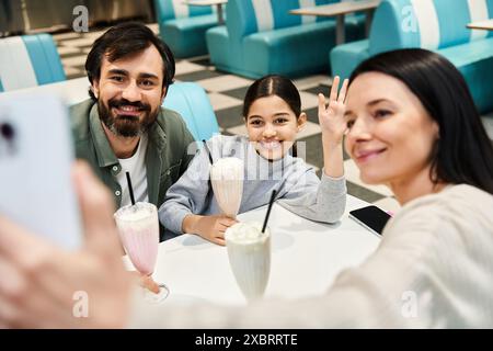 Eine fröhliche Familie fängt einen Moment zusammen ein und lächelt, während sie während ihres Wochenendausflugs in einem charmanten Retro-Diner ein Selfie macht. Stockfoto