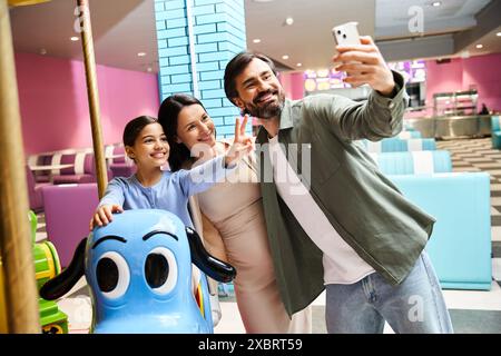 Eine fröhliche Familie lächelt, während sie am Wochenende ein Selfie vor einem Karussell in einer Spielzone in den Einkaufszentren macht. Stockfoto