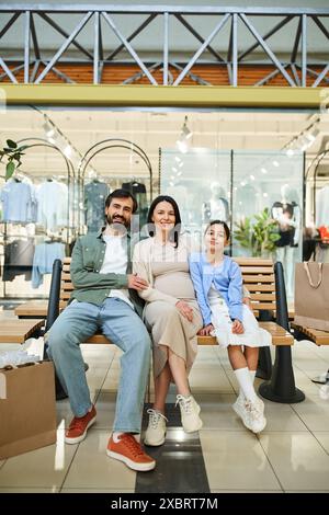 Eine Familie, die an einem Wochenende auf einer Bank in einem geschäftigen Einkaufszentrum lächelt und sich entspannt. Stockfoto