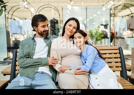 Eine schwangere Frau und ihre Tochter sitzen auf einer Bank in einem Einkaufszentrum und genießen während ihres Einkaufswochenendes einen Bonding-Moment. Stockfoto