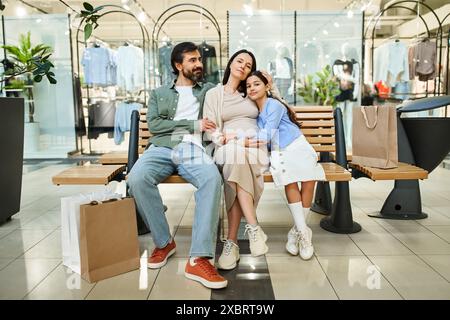 Eine schwangere Frau und ihre Tochter verbringen einen zärtlichen Moment, während sie auf einer Bank in einem geschäftigen Einkaufszentrum sitzen. Stockfoto