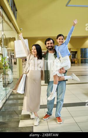 Eine glückliche Familie mit einem Baby trägt Einkaufstaschen, während sie bei einem Wochenendausflug durch ein geschäftiges Einkaufszentrum schlendert. Stockfoto