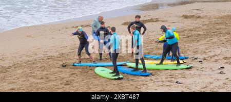 Surflehrer führen Lehrer aus dem Surf Sanctuary und unterrichten eine Gruppe von Surfanfängern am Fistral Beach in Newquay in Cornwall, Großbritannien Stockfoto