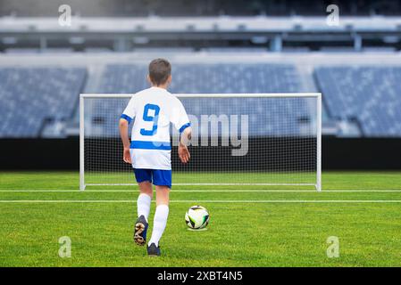 Ein junger Fußballspieler, der in einem modernen Stadion einen Elfmeterschuss auf ein leeres Tor wirft, hält die Spannung des Spiels fest Stockfoto