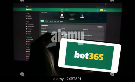 Person, die ein Mobiltelefon mit dem Logo des britischen Sportwettenunternehmens Bet365 vor der Business-Webseite hält. Schwerpunkt auf dem Display des Telefons. Stockfoto