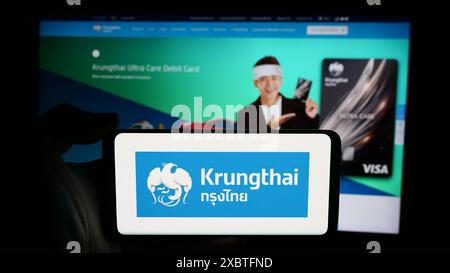 Person mit Handy mit Logo des thailändischen Unternehmens Krungthai Bank Public Company Limited vor der Webseite. Schwerpunkt auf dem Display des Telefons. Stockfoto