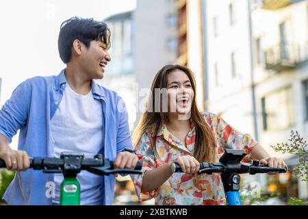 Lächelndes junges Paar mit Elektrorollern in der Stadt Stockfoto