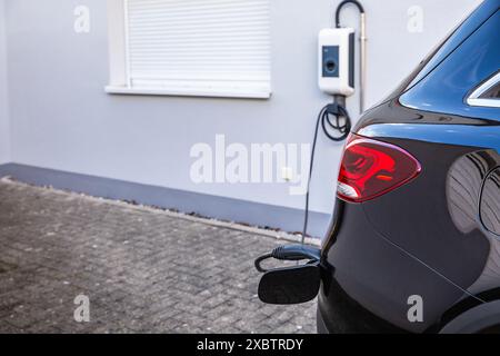 Ein Hybrid-Elektrofahrzeug wird von einem Wallbox in einem modernen Wohnhaus aufgeladen Stockfoto