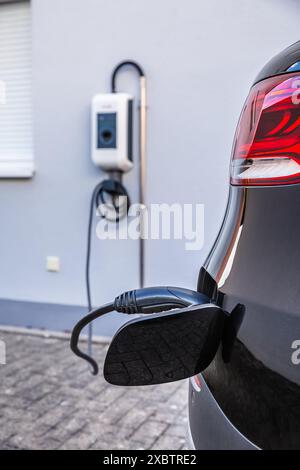 Ein Hybrid-Elektrofahrzeug wird von einem Wallbox in einem modernen Wohnhaus aufgeladen Stockfoto