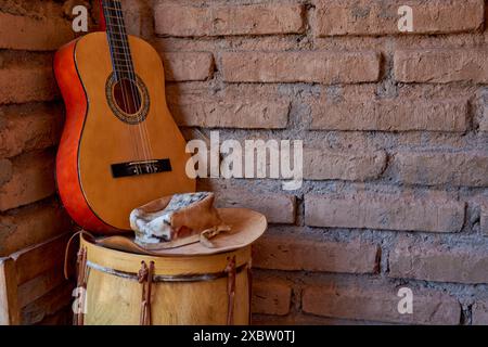 Klassische Criollo-Gitarre auf einer Trommel und einem Hut, im Hintergrund eine Ziegelmauer, in Salta, Argentinien. Stockfoto