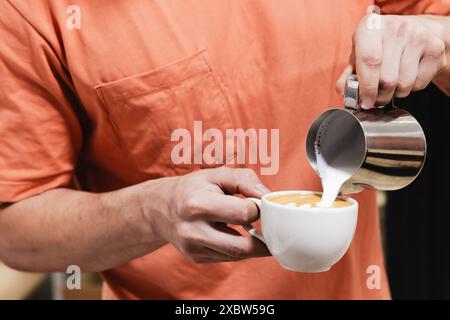 Hände eines Barista, der Cappuccino mit einer Latte Art in einem weißen Becher zubereitet Stockfoto