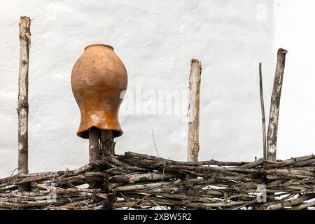 Ein alter traditioneller Tonkrug befindet sich auf einem Holzzaun vor der weißen Landhausmauer Stockfoto