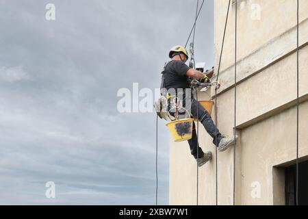 Akrobatik-Seilbau-Angestellter, der mitten in der Luft steht und an einer Fassade arbeitet. Stockfoto